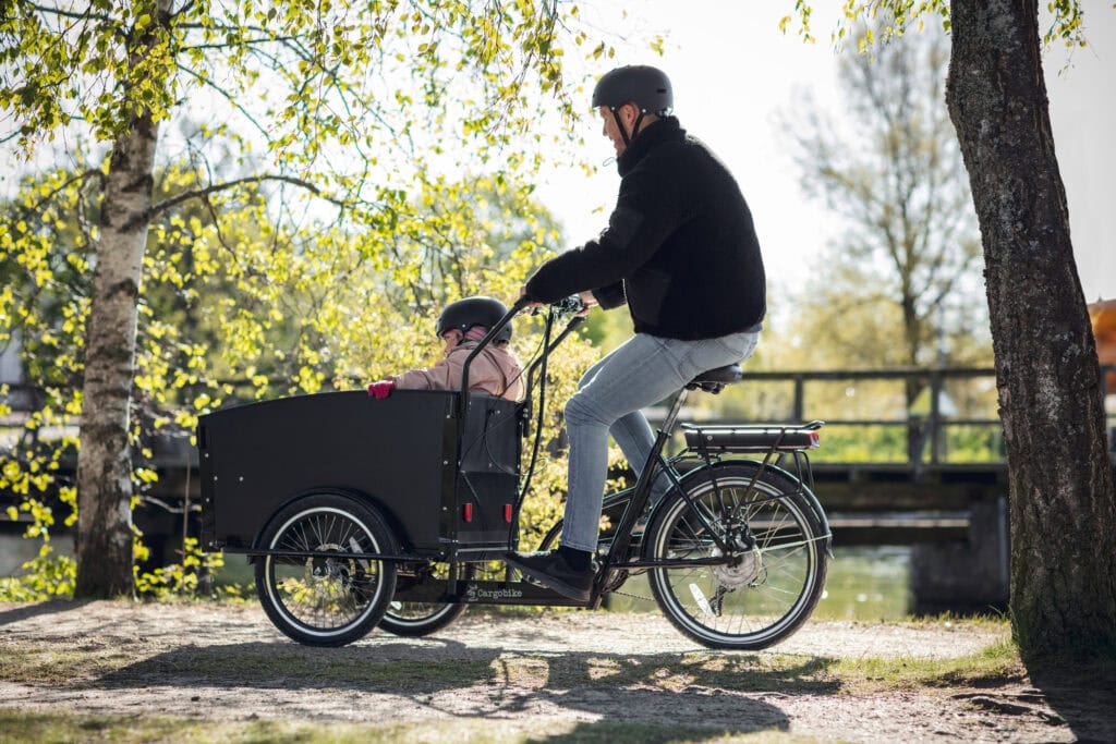 Vuxen och barn cyklar lådcykel på Vårvik.